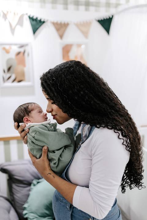 Mãe segurando o bebê no colo e aproximando o rosto para um carinho.'