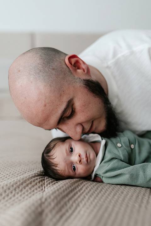Pai inclinando o rosto e encostando carinhosamente na cabeça do bebê.'