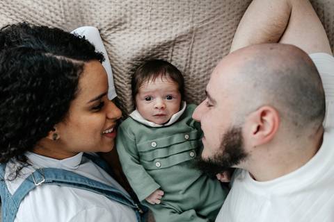 Vista superior da família deitada no sofá com o bebê entre o pai e a mãe.'