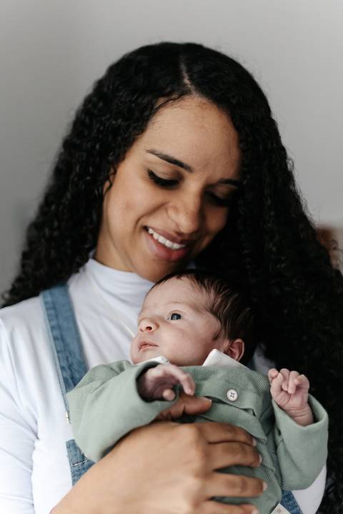 Mãe sorridente e carinhosa segurando o bebê acalentado em seus braços.'