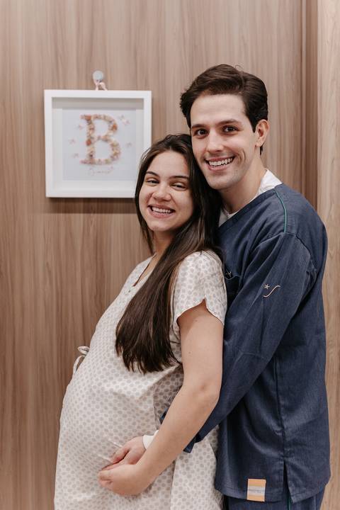 Retrato do casal sorridente abraçado no quarto da maternidade.'