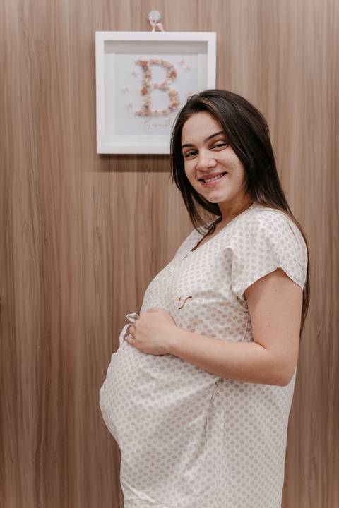 Gestante sorrindo no quarto de hospital enquanto acaricia a barriga.'