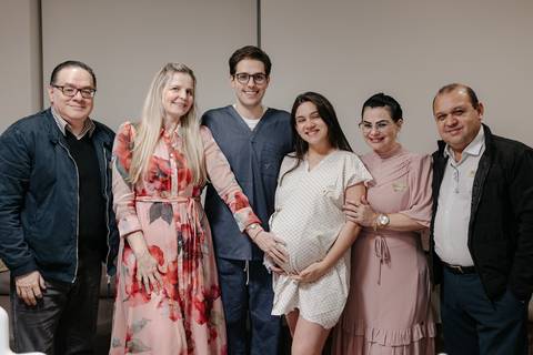 Foto em grupo reunindo a família e acompanhantes ao redor da gestante na maternidade.'