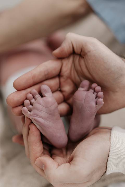 Mãos do pai e da mãe segurando com carinho os pezinhos do bebê.'