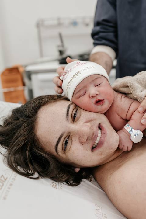 lose-up da mãe sorrindo radiante com o bebê apoiado ao lado de seu rosto.'