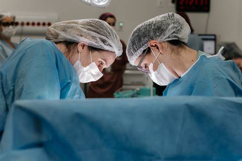 Equipe médica com toucas e máscaras cirúrgicas atuando no procedimento do parto.'