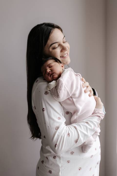 Mãe em plano médio segurando o bebê adormecido em seus braços.'
