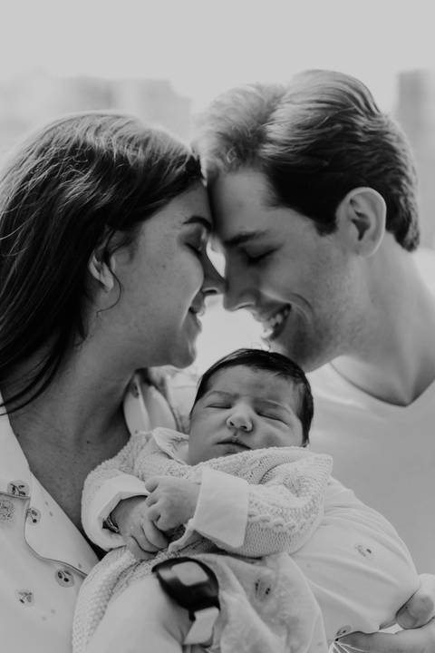 Versão em preto e branco do casal com os rostos próximos e sorrindo sobre o bebê.'