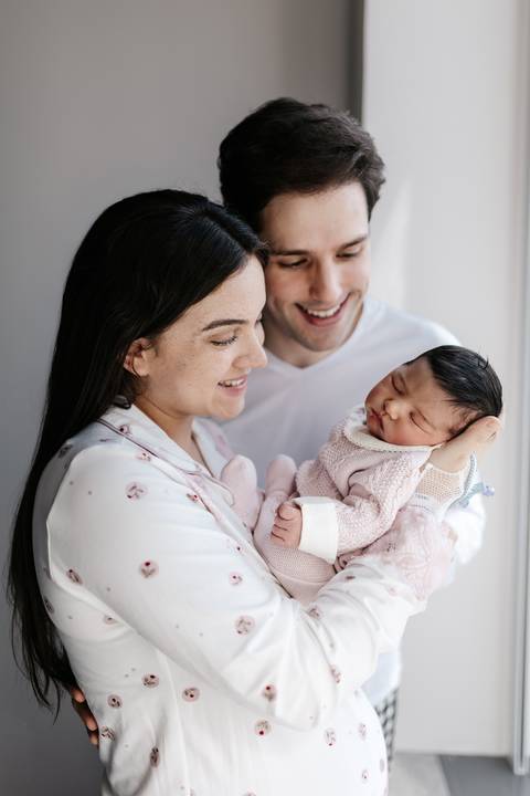 Pai e mãe olhando carinhosamente para o recém-nascido no colo.'
