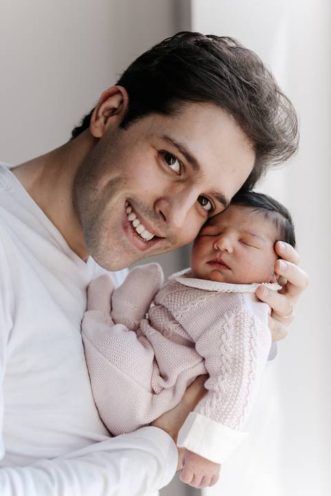 Retrato em close-up do pai sorrindo orgulhoso com o bebê deitado em seu peito.'