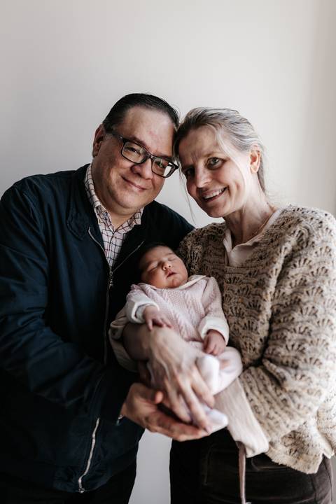 Retrato dos avós paternos sorrindo e segurando a neta recém-nascida no colo.'