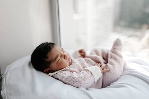 Bebê recém-nascido deitado confortavelmente em uma almofada perto da janela.'