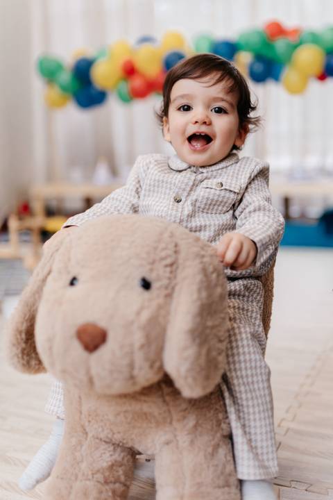 Bebê aniversariante montado em um urso de pelúcia gigante durante a festa.'