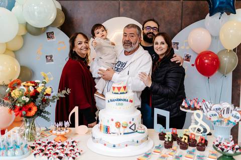 Foto em grupo com familiares reunidos atrás da mesa principal da festa.'
