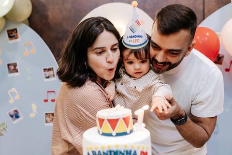 Pais e o aniversariante assoprando a vela de 1 ano no bolo de aniversário.'