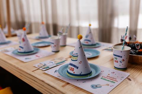 Decoração da mesa infantil com pratinhos, copos e chapéus de festa personalizados com notas musicais.'