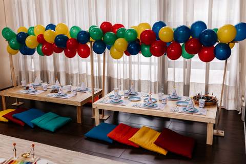 Decoração das mesas infantis baixas com almofadas coloridas no chão e arco de balões.'