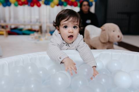 Aniversariante animado com os braços abertos brincando na piscina de bolinhas.'