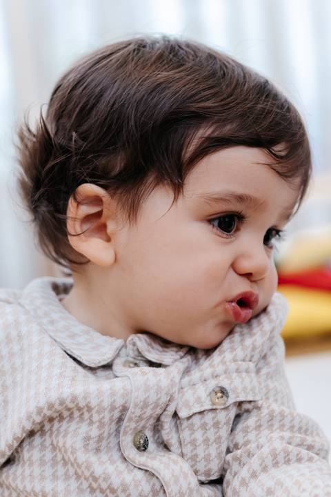 Retrato de perfil em plano fechado do bebê fazendo carinha fofa durante a celebração.'