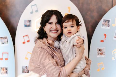 Mãe e filho sorrindo abraçados em frente ao painel de notas musicais.'