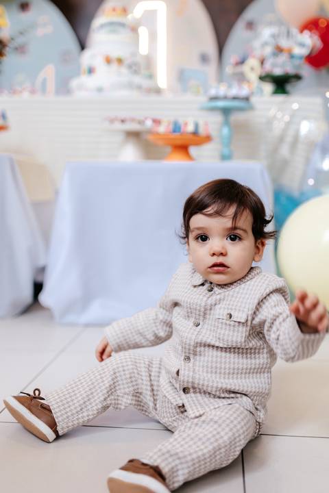 Plano médio do bebê sentado no chão olhando atento para a câmera.'
