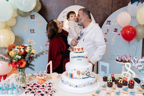 Avós e pais com o aniversariante no colo sorrindo juntos em frente ao painel decorativo.'