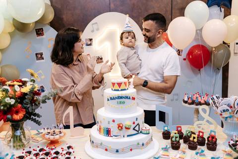 Pais com o aniversariante no colo em frente ao bolo de aniversário decorado no tema 