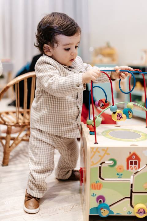 Detalhe das mãozinhas do bebê interagindo com o brinquedo aramado de madeira.'