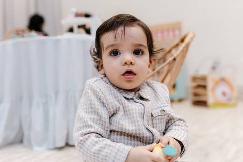 Aniversariante sentado no chão olhando diretamente para a câmera com olhar curioso.'