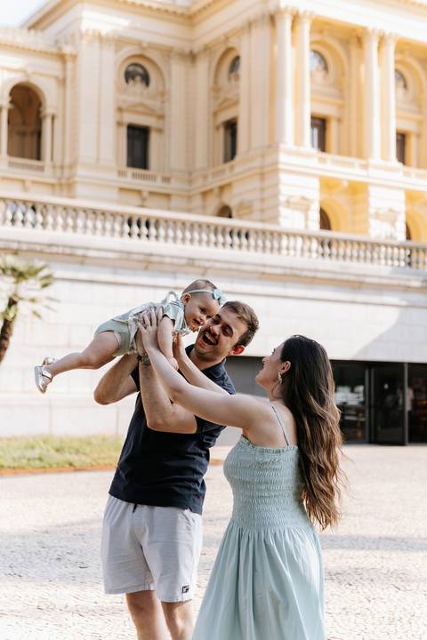 Pais levantando a filha pequena no ar em frente à fachada do Museu do Ipiranga.'