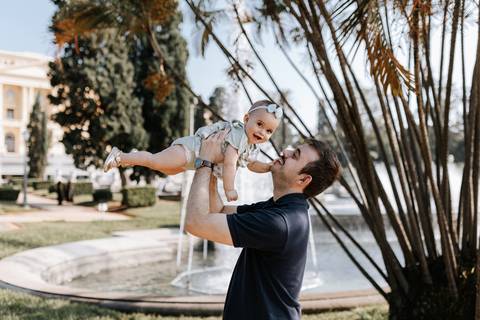 Pai erguendo a bebê no ar em momento divertido ao ar livre.'