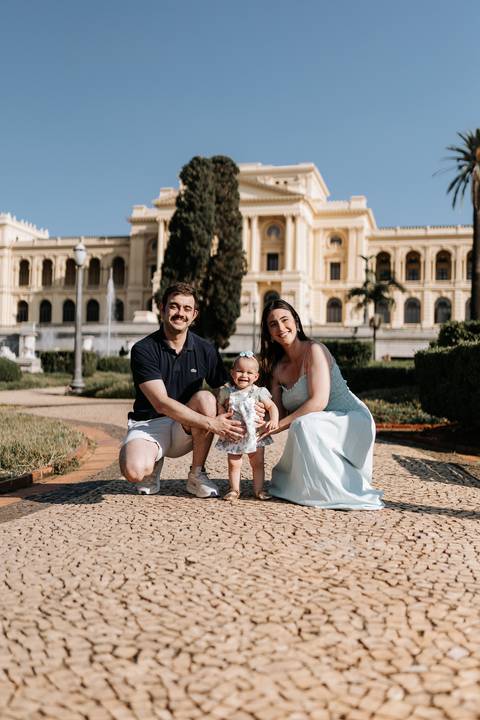 Retrato de família completo posando ajoelhados no jardim em frente ao imponente Museu do Ipiranga.'