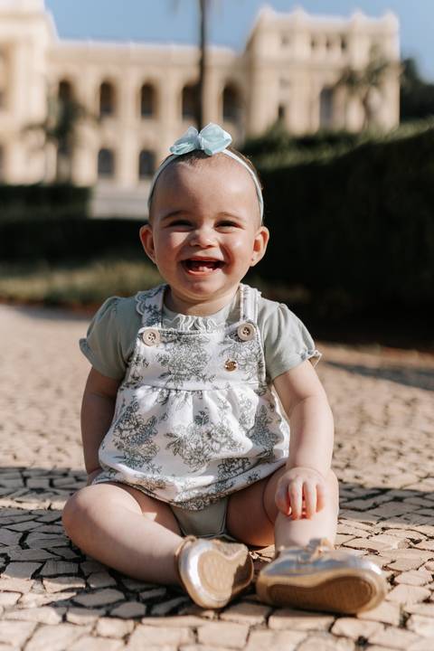 Close-up da bebê sorrindo alegremente de macacão estampado e laço na cabeça.'