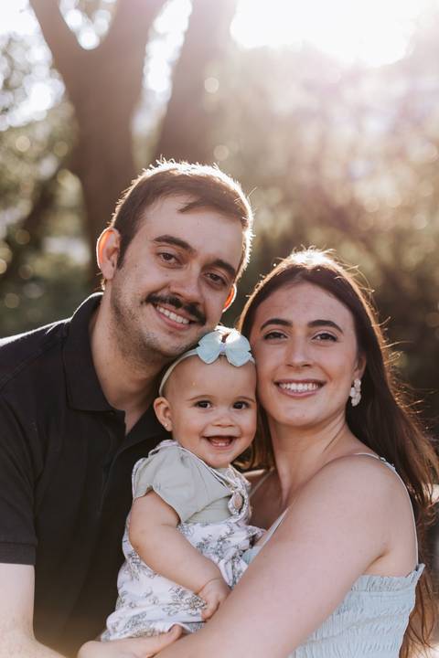 Retrato em close-up do casal com a bebê de rostos colados e sorridentes.'