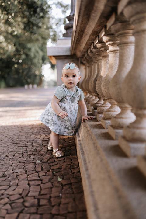 Bebê em pé se apoiando na mureta de pedra clássica do parque.'