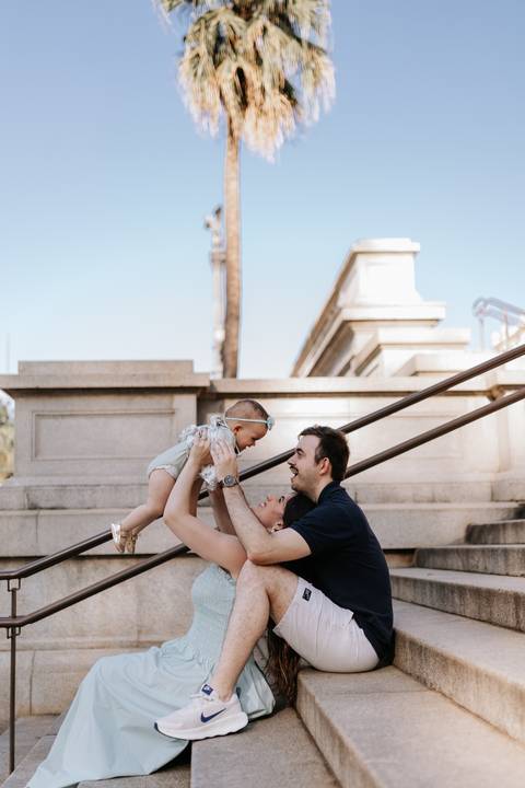 Pai erguendo a bebê no ar perto do corrimão da escadaria do museu.'