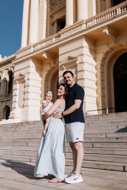 Retrato da família em pé posando na imponente escadaria do Museu do Ipiranga.'