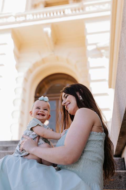 Mãe e filha sorrindo juntas em ângulo contraponto em frente aos arcos do museu.'