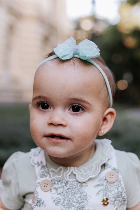 Retrato em plano fechado da bebê de laço olhando curiosa para a câmera.'