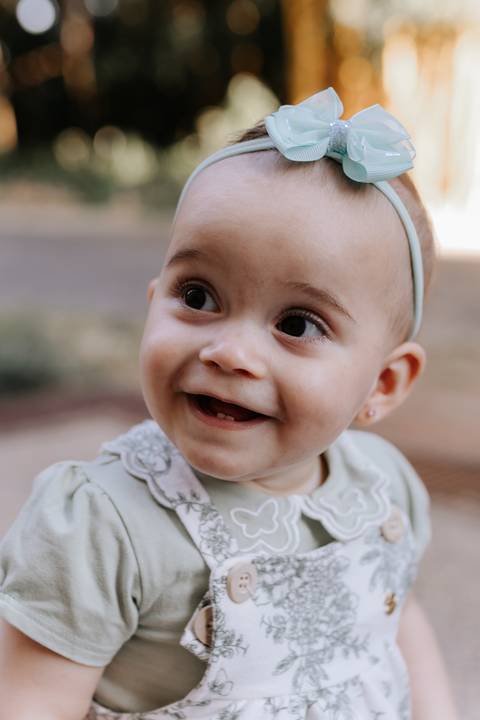 Retrato em plano médio da bebê sorrindo radiante de macacão estampado.'