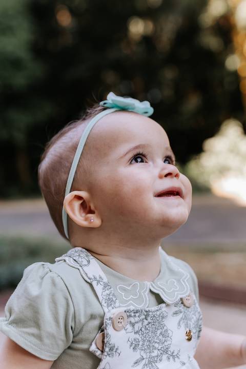 Plano médio de perfil da bebê olhando para o alto com luz natural destacando seu rosto.'
