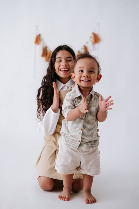 Bebê sorridente batendo palminhas no colo da irmã mais velha.'