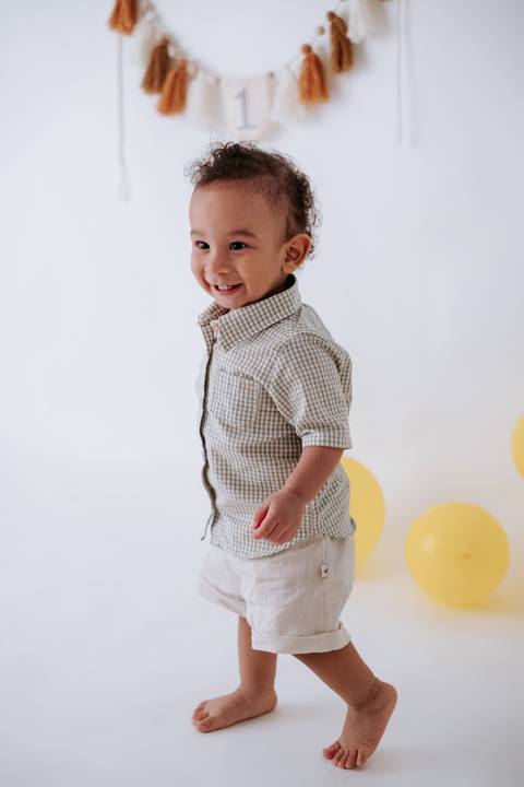 Menino pequeno em pé de perfil sorrindo espontaneamente durante o ensaio.'