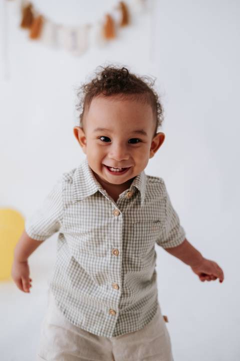 Plano fechado do bebê sorrindo alegremente com os balões amarelos ao fundo.'