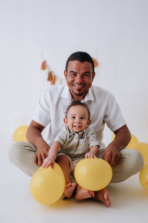 Pai sentado no chão com o bebê sorridente entre suas pernas.'