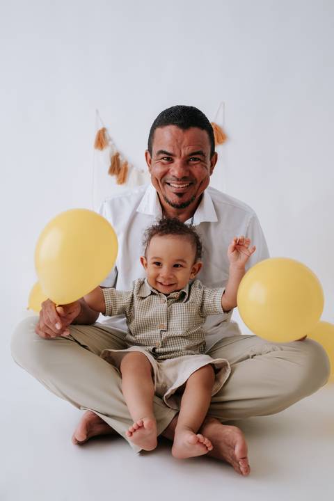 Pai e bebê brincando com balões amarelos.'
