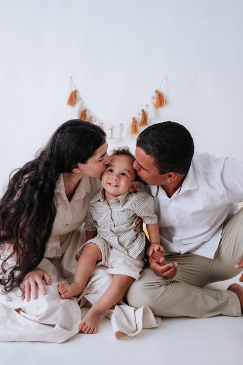 Pais dando um beijo carinhoso nas bochechas do bebê ao mesmo tempo.'