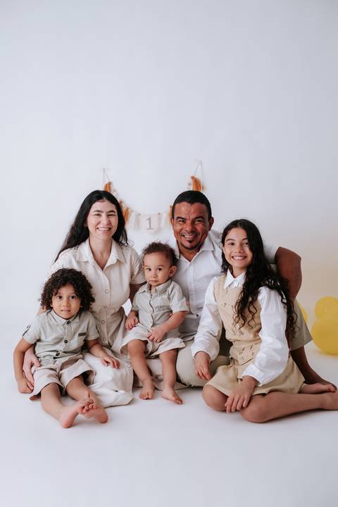 Retrato oficial da família reunida no chão do estúdio, todos sorrindo para a câmera.'