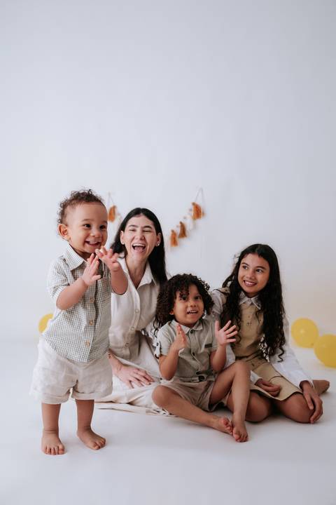 Mãe e os três filhos brincando e interagindo animados, com o bebê gesticulando com as mãos.'