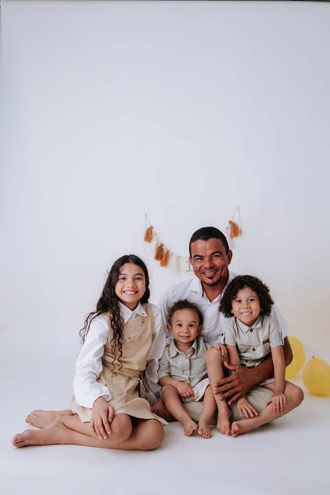 Pai abraçado aos três filhos sorrindo alegremente juntos no estúdio.'